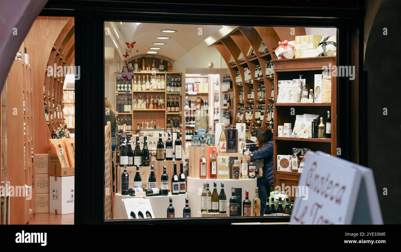 I visitatori esplorano un'affascinante enoteca ad Alba, in Italia, circondata da scaffali pieni di una vasta gamma di vini locali e prodotti gastronomici gourmet, creando un del Foto Stock