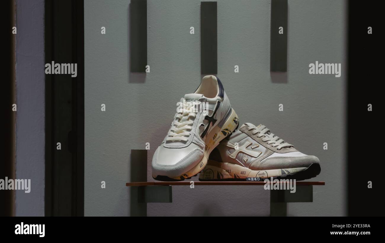 Un paio di sneaker eleganti è impreziosito da un elegante ripiano in legno all'interno di un negozio alla moda di Alba, Italia. La luce del pomeriggio mette in risalto il loro design Foto Stock