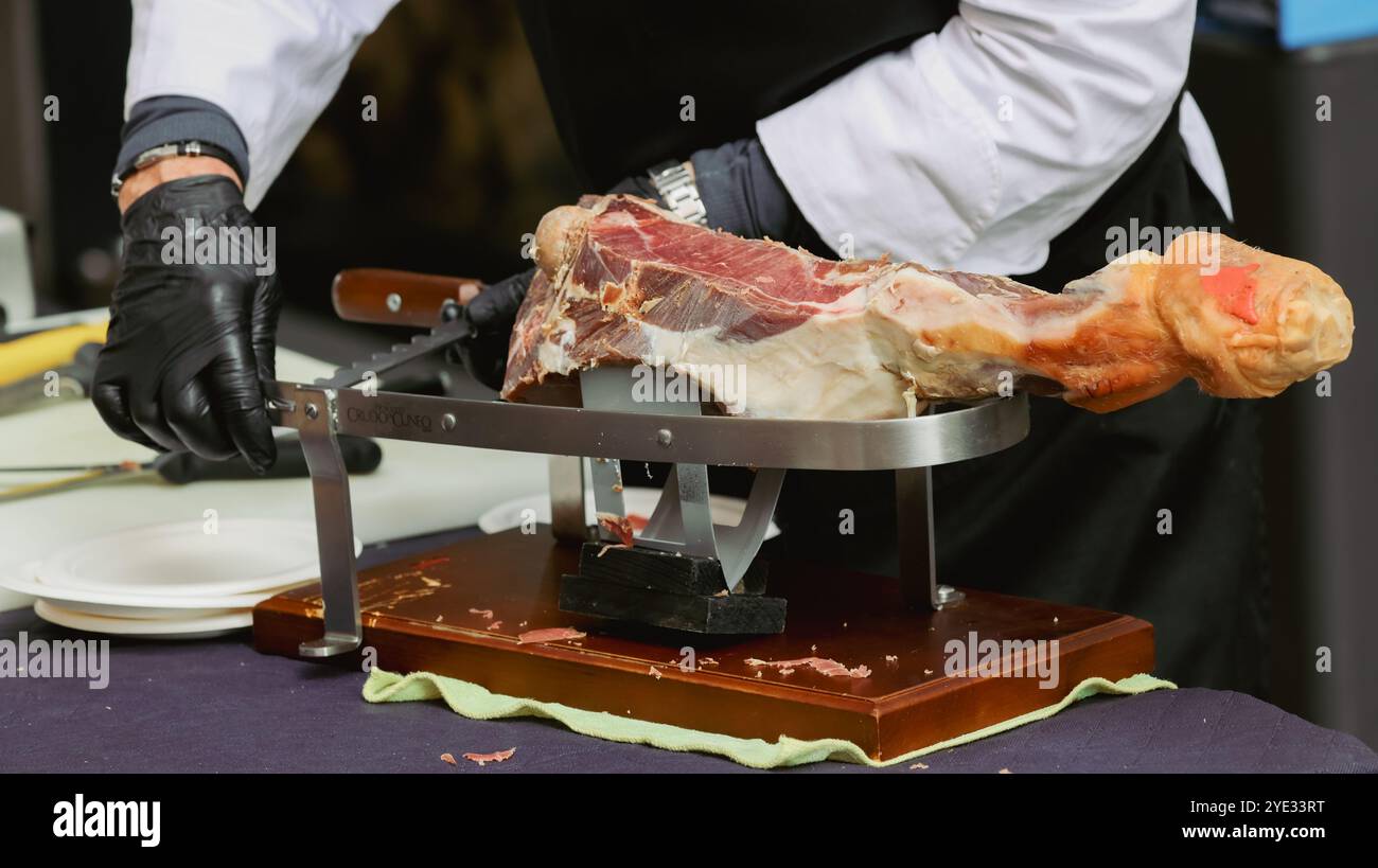 Uno chef esperto affetta sapientemente una grande coscia di salumi ad Alba, Italia. Gli ospiti si riuniscono per assistere a questa arte culinaria Foto Stock