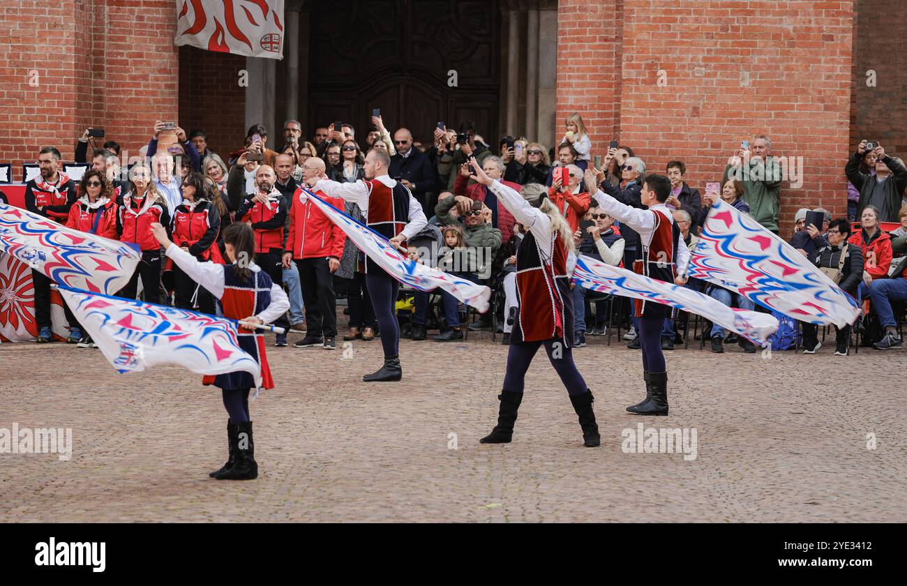 Gli artisti in un abbigliamento vivace fanno sventolare grandi bandiere in motivi intricati mentre intrattiene un pubblico affascinato ad Alba. Foto Stock