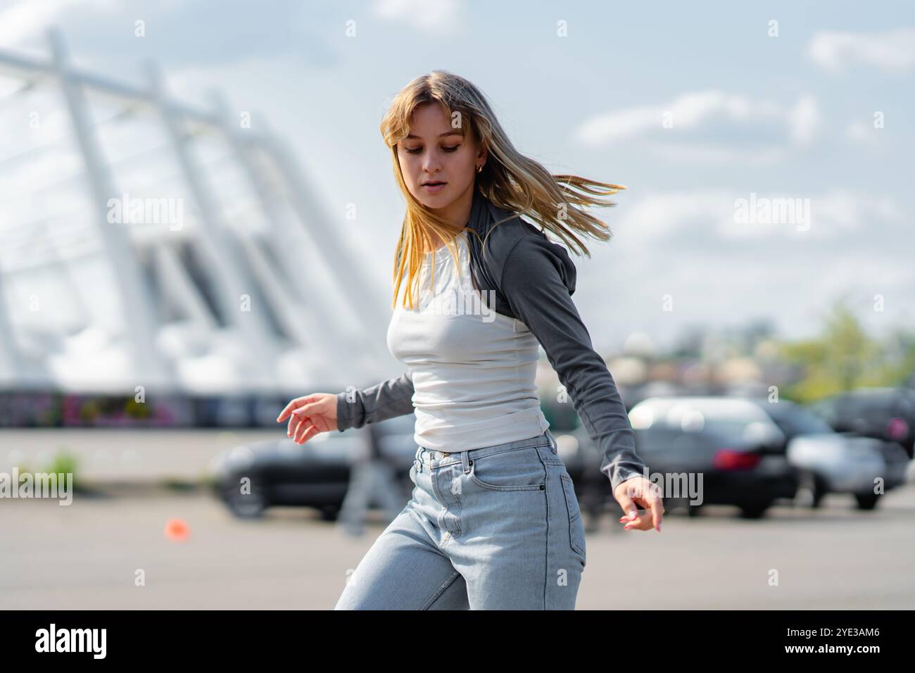 Giovane donna che balla in un outfit casual vicino alle auto parcheggiate in una giornata di sole Foto Stock