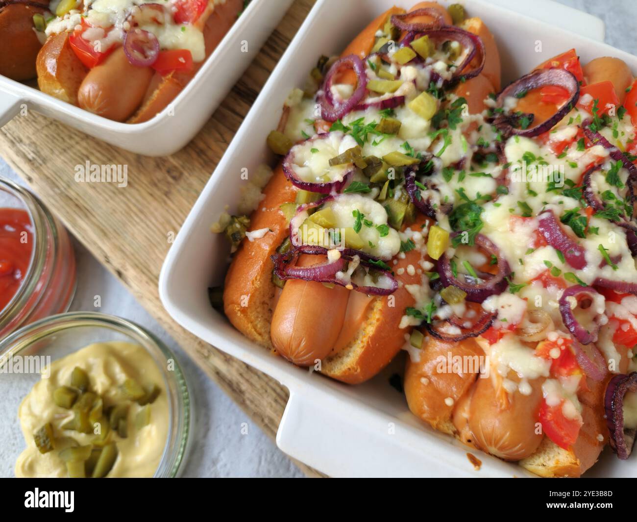 Hot Dogs al forno con formaggio fuso, cipolle rosse, pomodori e crocchette nel piatto da forno Foto Stock