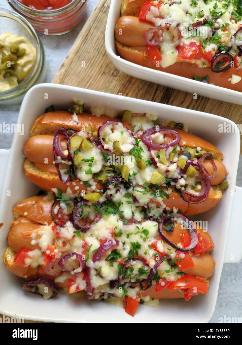 Hot Dogs al forno con formaggio fuso, cipolle rosse, pomodori e crocchette nel piatto da forno Foto Stock
