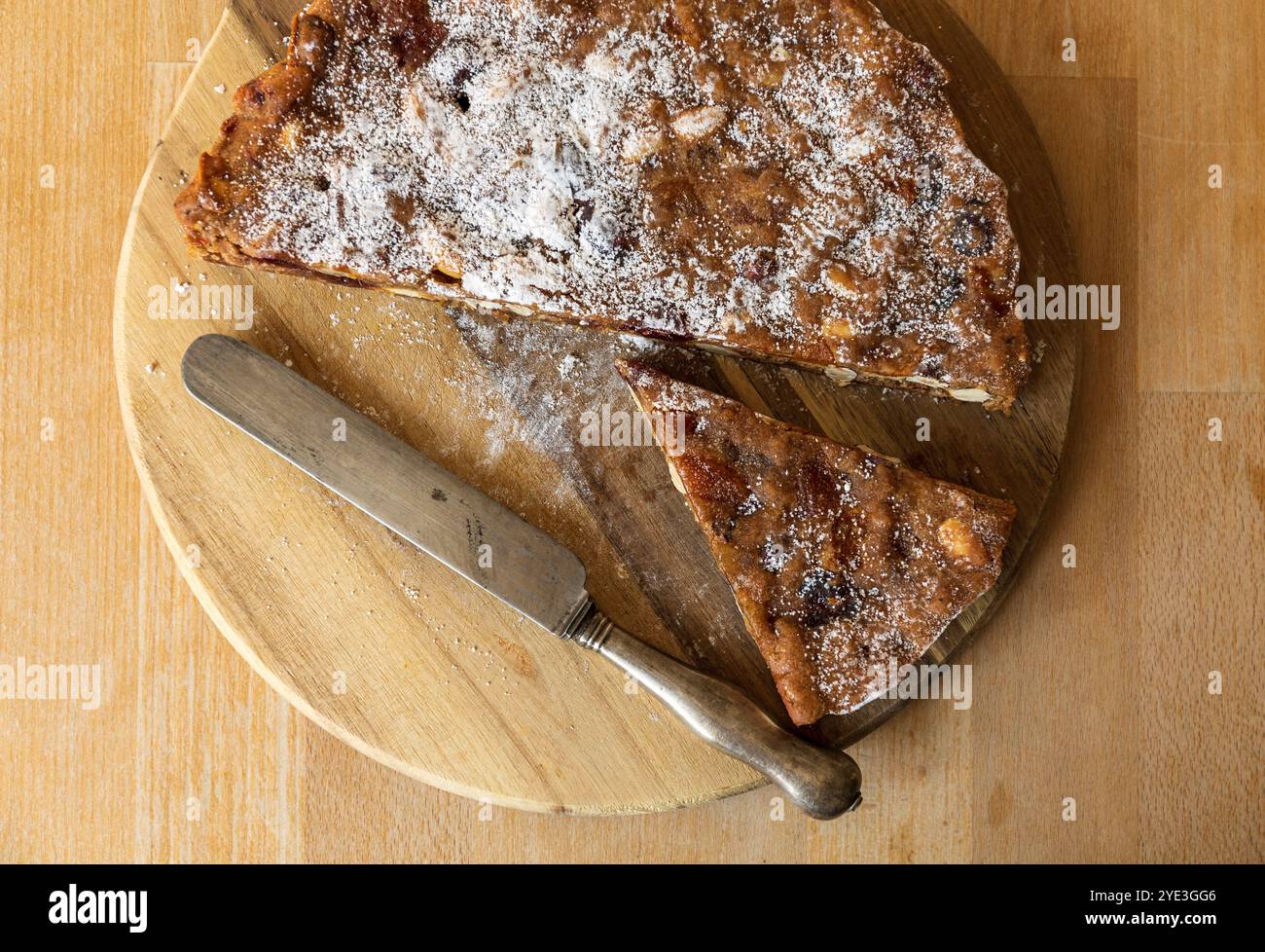 Fotografia da tavolo di un tradizionale panforte da dessert italiano a fette su un tagliere di legno con un coltello antico Foto Stock
