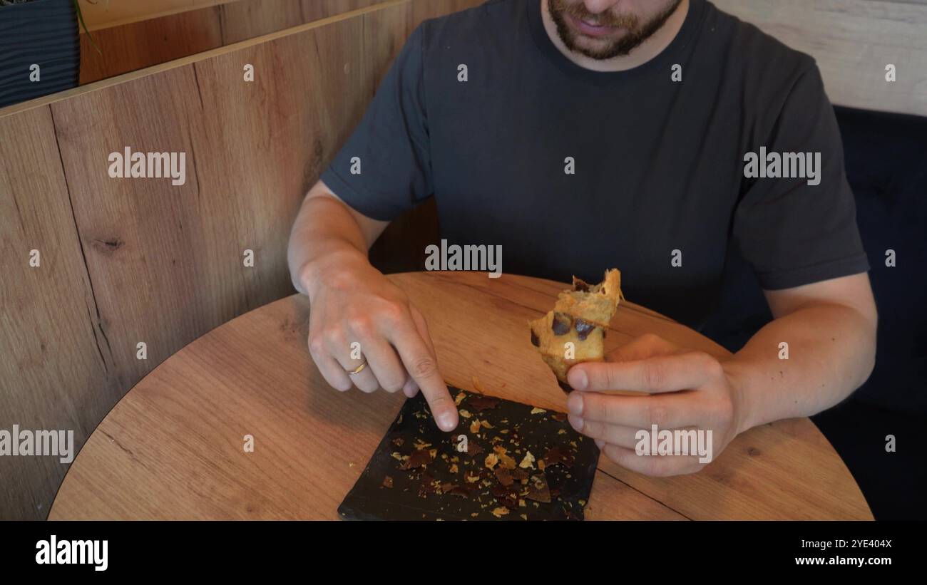 La scena mostra un croissant su una lavagna nera, con la mano di un giovane che tiene un pezzo di pasta morsa. Il video trasmette l'appeal del forno appena sfornato Foto Stock