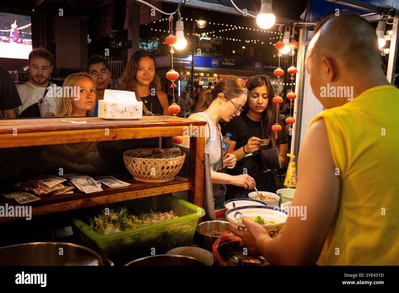 Clienti stranieri che acquistano spaghetti da un venditore al mercato notturno di Luang Prabang. Foto Stock