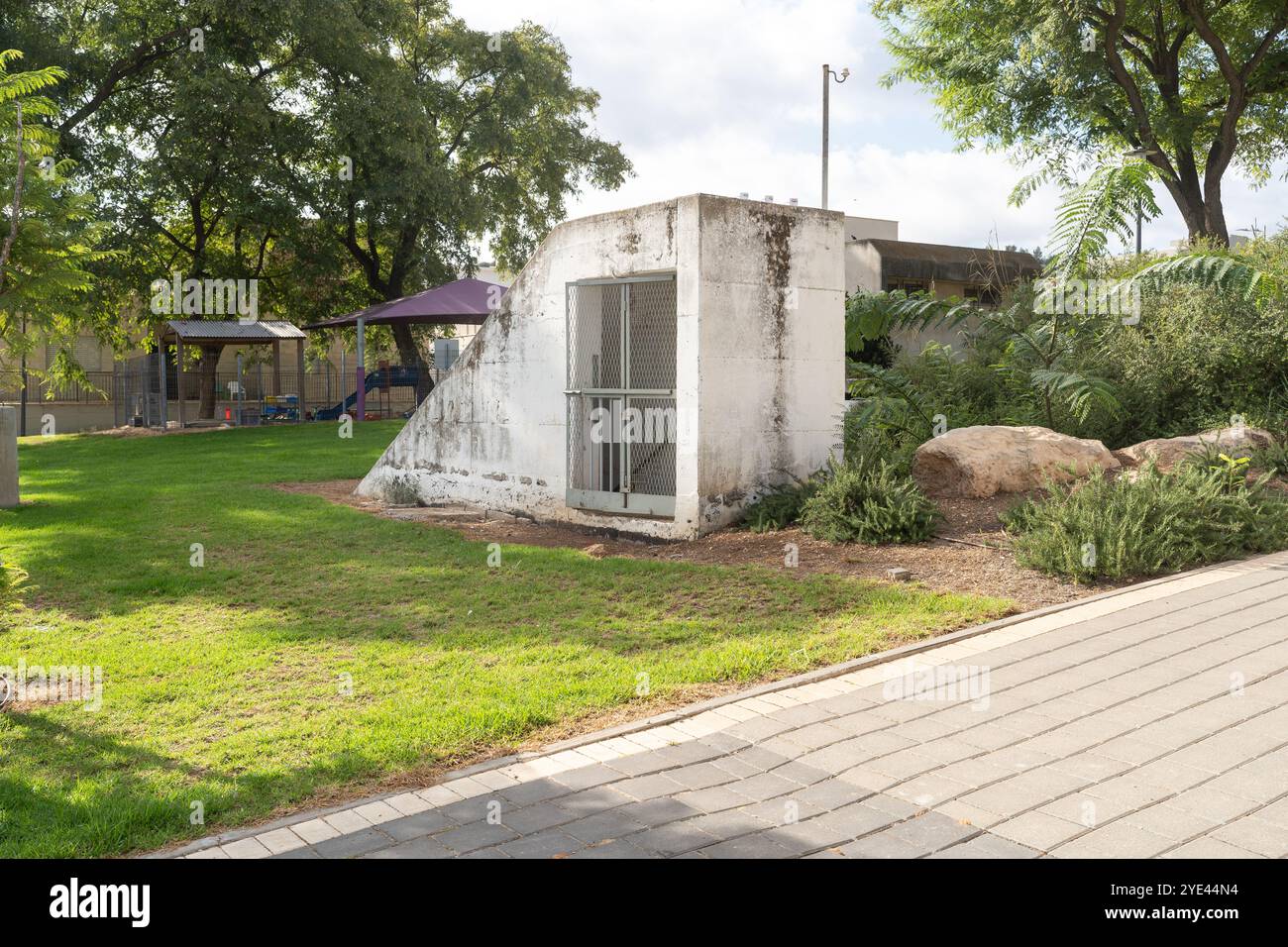 Un rifugio antiatomico in cemento situato in un tranquillo quartiere di Israele, che si fonde con il verde circostante. Questa struttura riflette l'esigenza di sicurezza negli ambienti di uso quotidiano. Foto Stock