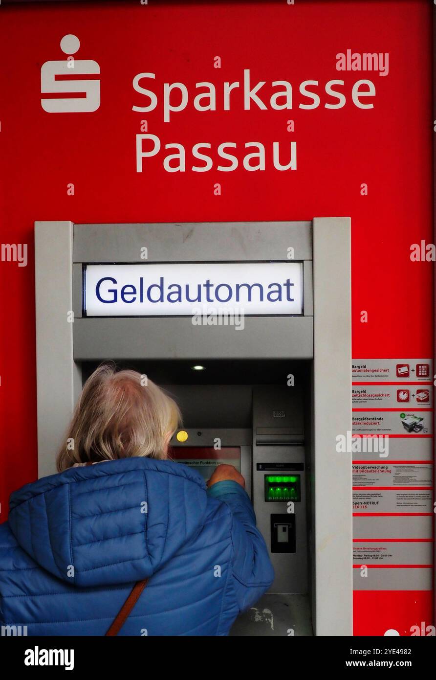 Passau, Germania - 29 ottobre 2024: Una donna di mezza età ritira denaro da uno sportello Bancomat della Banca Sparkasse Foto Stock