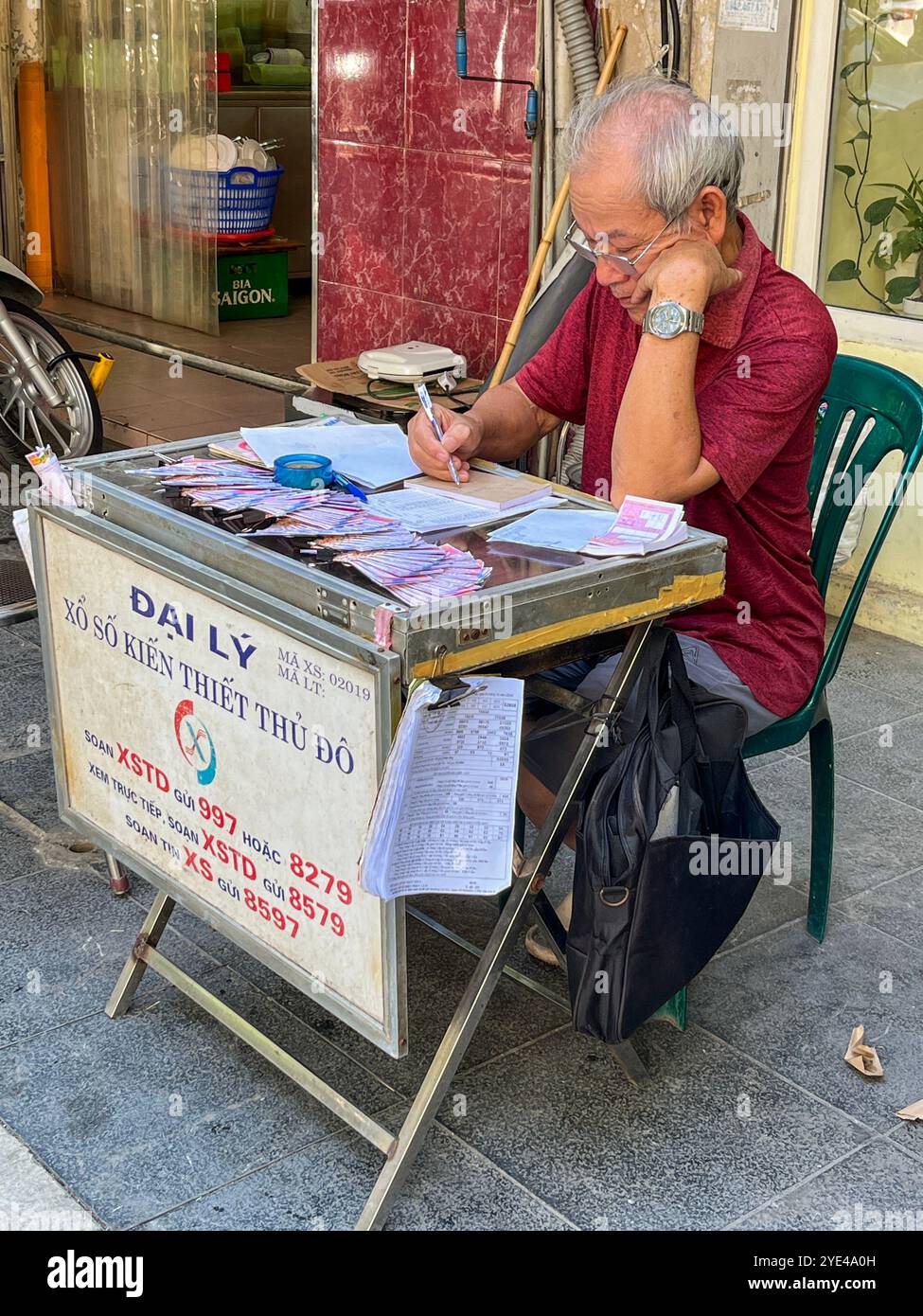 Hanoi, Vietnam: Vita quotidiana vietnamita, un anziano che vende biglietti della lotteria in una bancarella per le strade della capitale Foto Stock