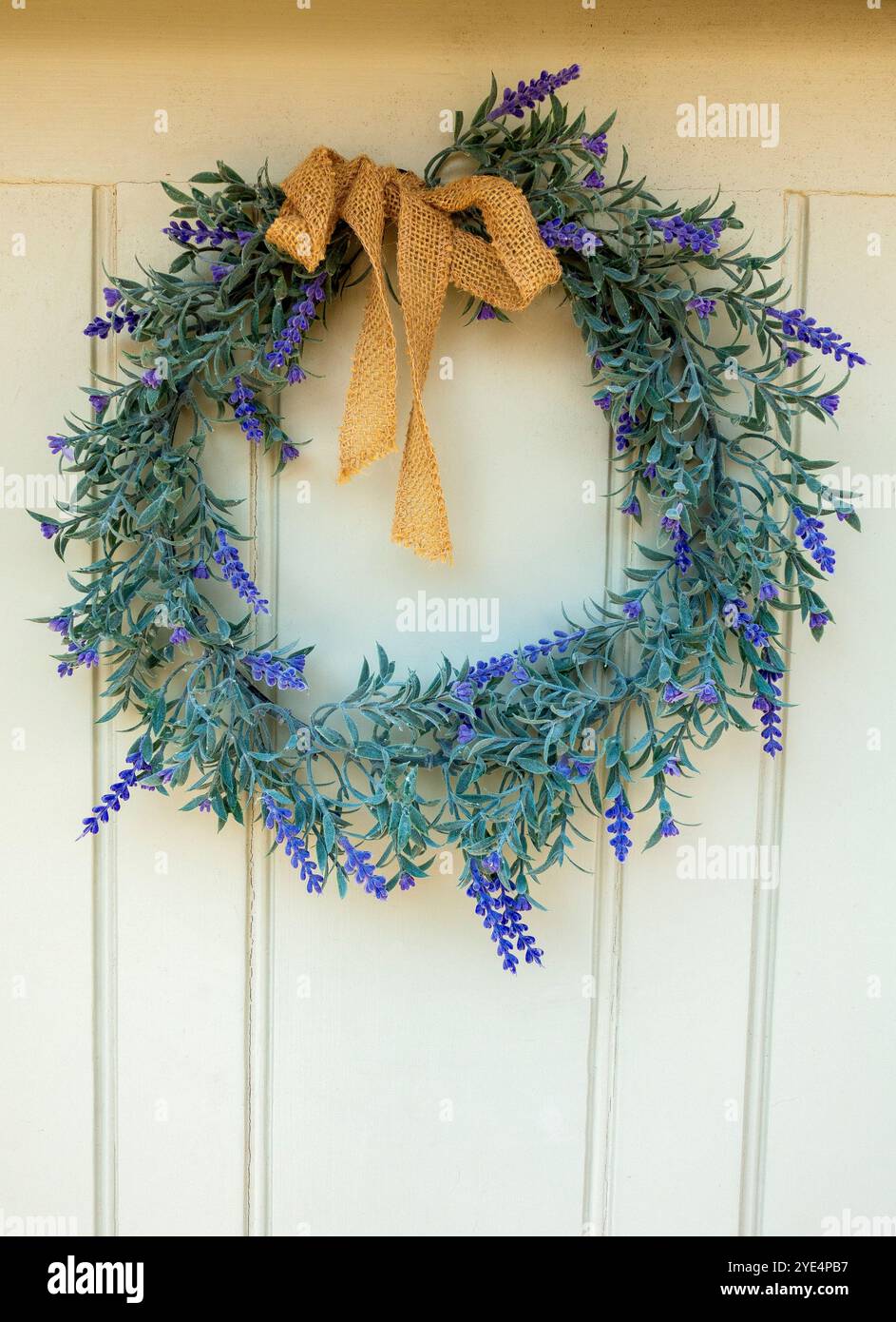 Appesa graziosamente su una porta rustica in legno, questa affascinante corona di lavanda affascina con la sua vegetazione lussureggiante e i delicati fiori viola Foto Stock