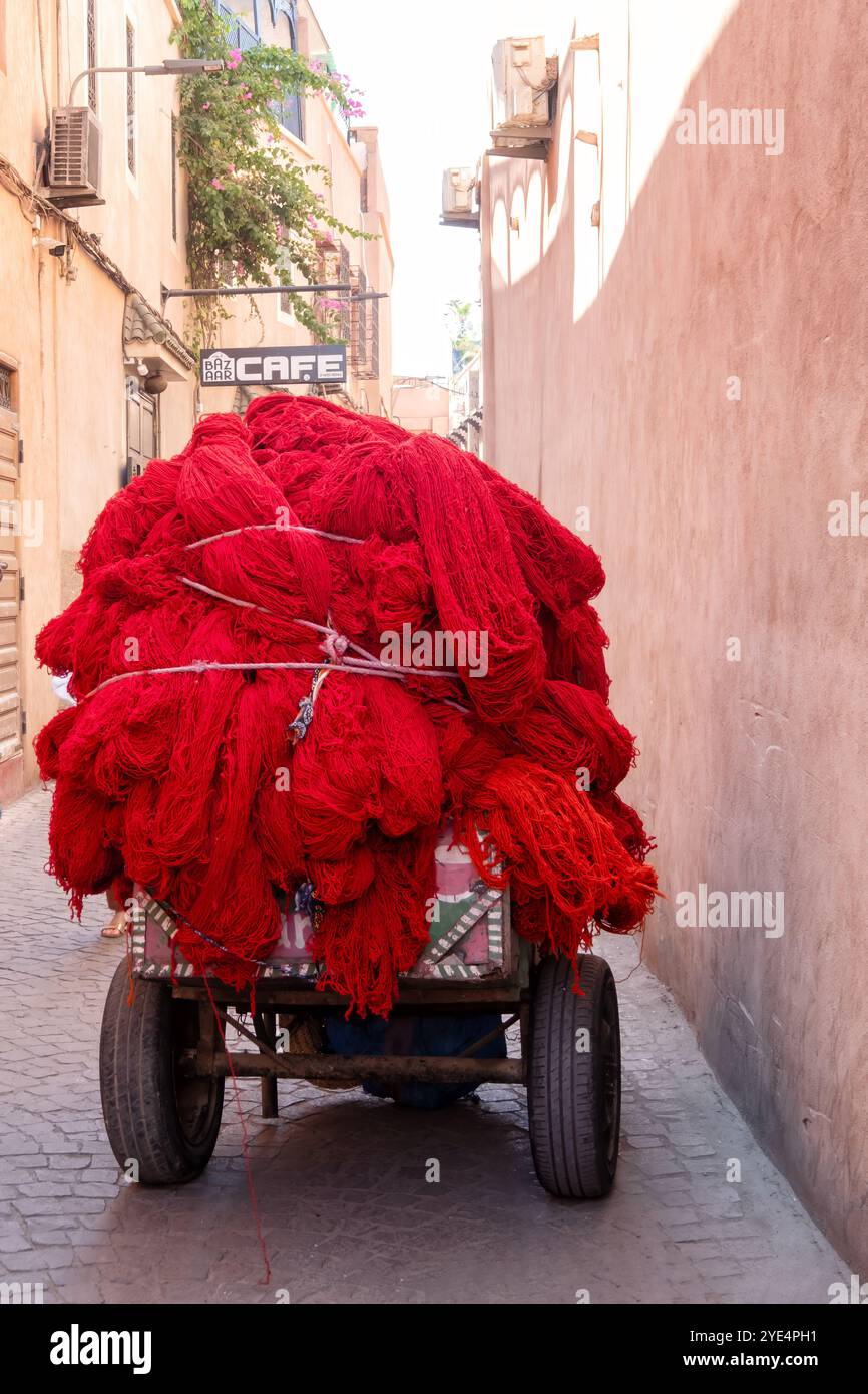 Marrakech, Marocco. Un carrello a mano carico di lana tinta rossa viene trasportato attraverso i suk centrali nella medina di Marrakech o nella città vecchia Foto Stock