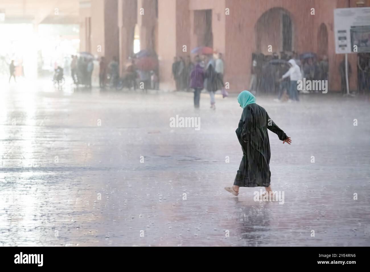 Marrakech, Marocco, Una donna bagnata che fa il pieno di acqua cammina attraverso Jemaa el-Fnaa, la piazza principale della città vecchia della medina di Marrakech durante un temporale e una forte pioggia Foto Stock