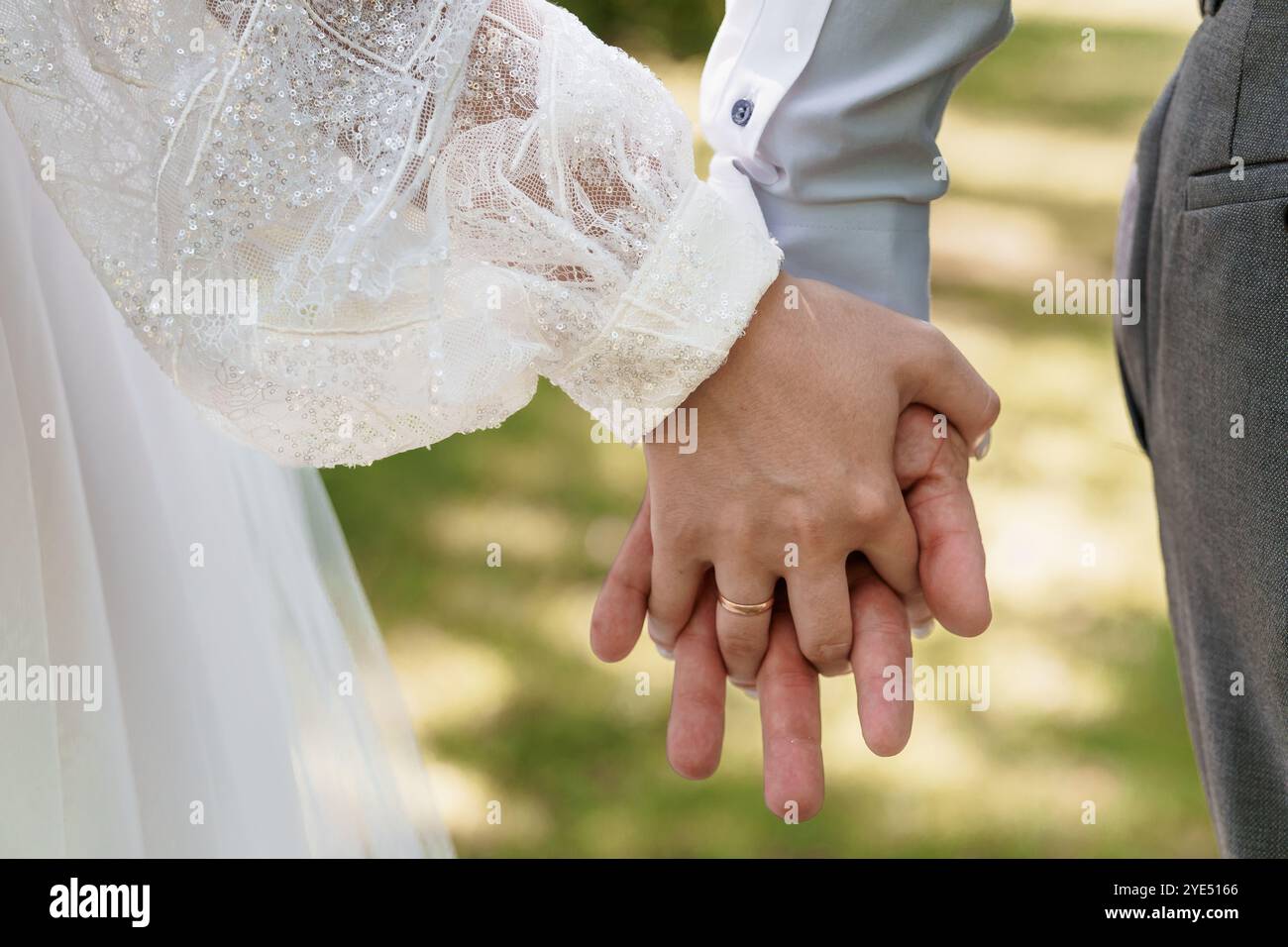 Intimo momento di una sposa e di uno sposo che si tengono per mano in un lussureggiante ambiente all'aperto. Foto Stock