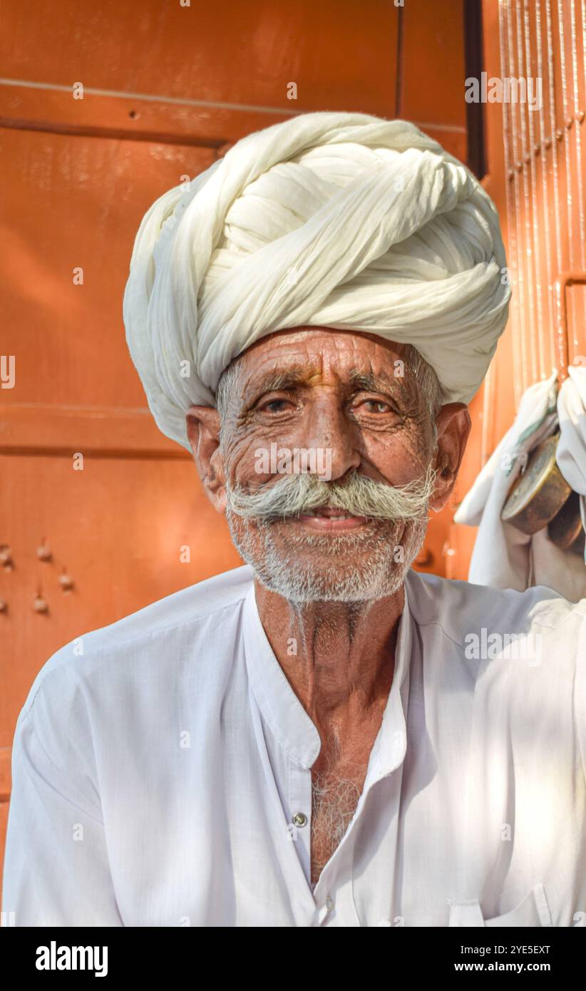 Uomo anziano con turban Rajasthan tradizionale sorridente felice guardando la fotocamera con toni caldi arancioni sullo sfondo Foto Stock