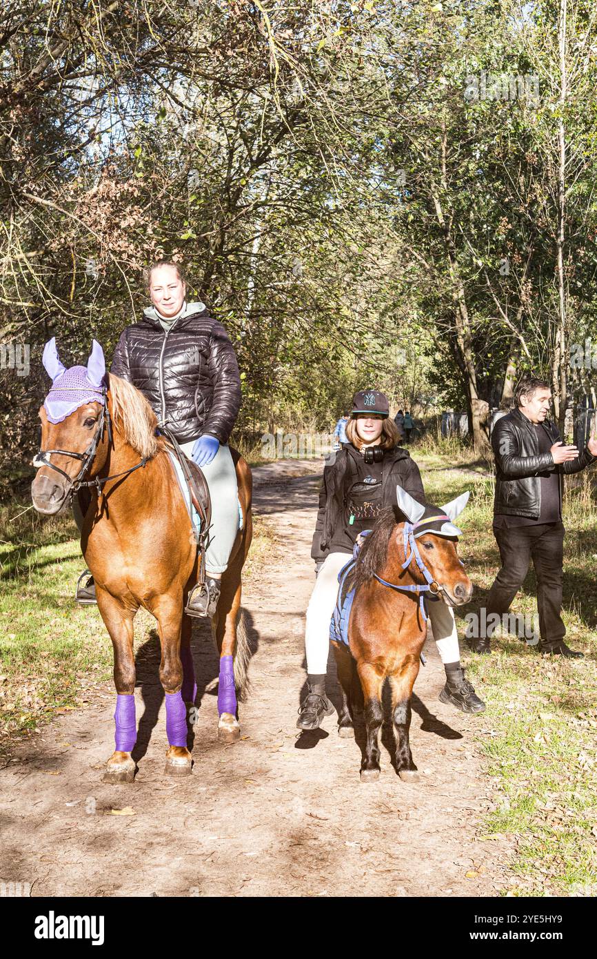 Due amiche, una più grande e una più giovane, una a cavallo, una a cavallo, una a cavallo nel vicolo in una soleggiata giornata autunnale, come Don Chisciotte e Sancho Panza. Foto Stock