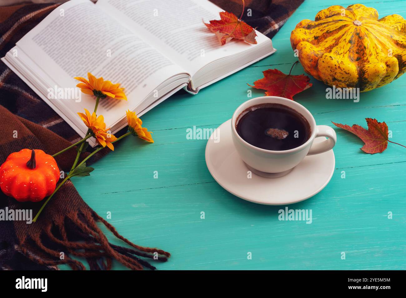 Tazza da caffè, zucche, foglie autunnali e libro su un tavolo di legno blu. L'autunno, il concetto del Ringraziamento. Vista dall'alto. Foto Stock