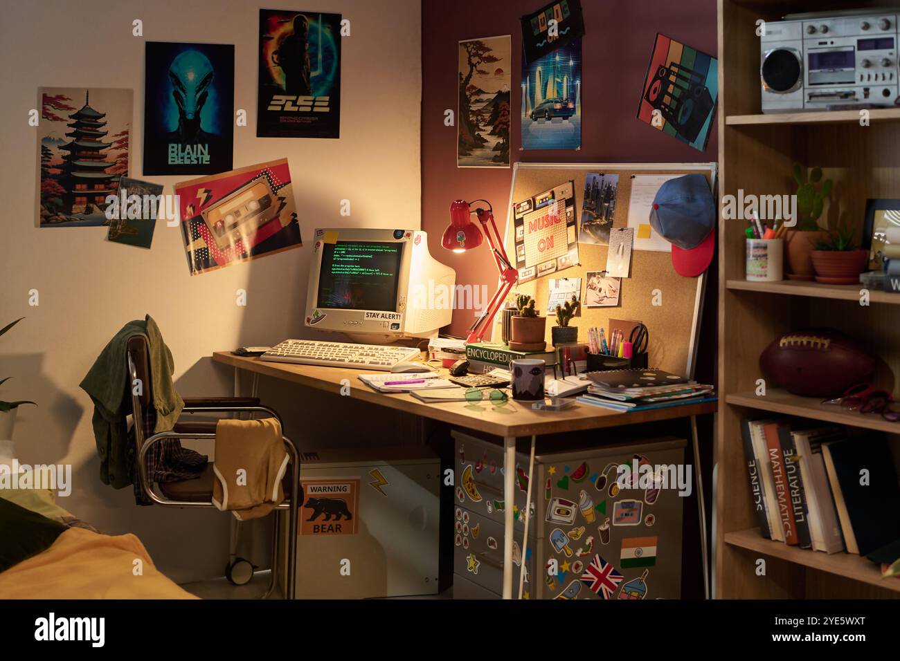 Computer retrò sulla scrivania decorato con poster vintage, vari strumenti di scrittura e oggetti personali che creano un'atmosfera nostalgica Foto Stock