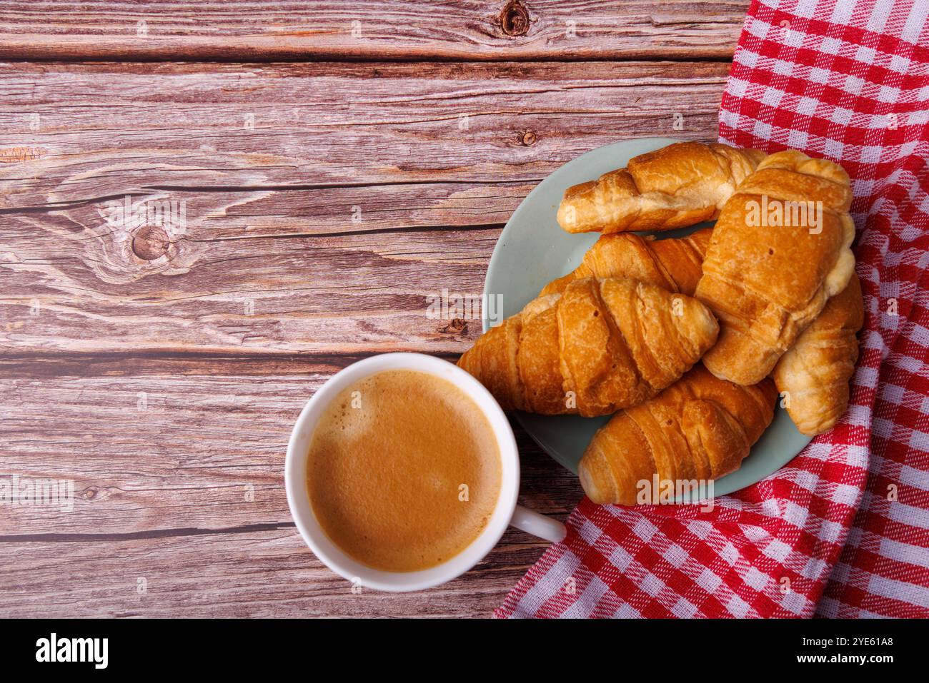 Un colpo di croissant e caffè su un tavolo di legno chiaro, che offre un momento accogliente per la colazione con dolci freschi e una bevanda calda. Foto Stock