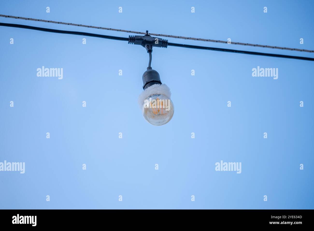 Una lampadina isolata si danneggia da un cavo contro un cielo blu brillante, creando un punto focale semplice ma sorprendente in uno spazio all'aperto durante il giorno Foto Stock