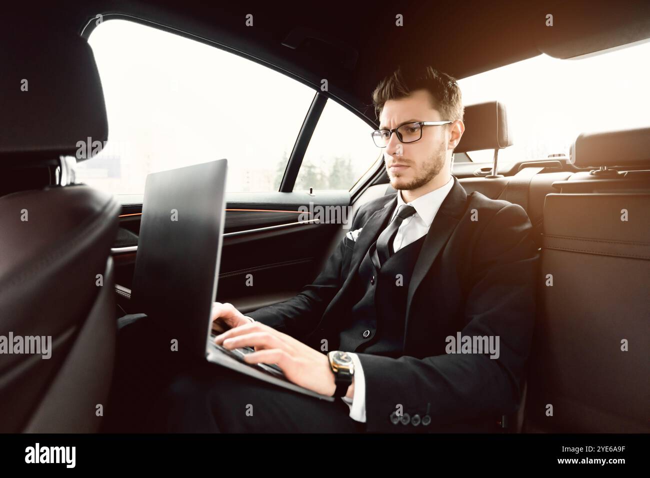 Uomo d'affari serio occupato utilizzando il suo laptop in auto di lusso Foto Stock