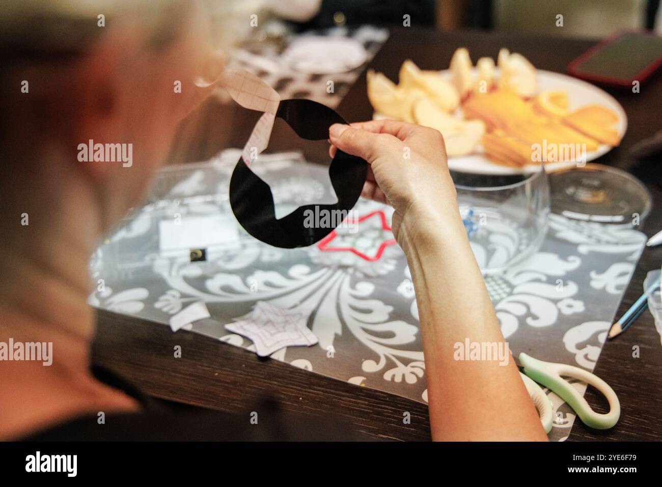 Attività di artigianato natalizio, tenendo con cura un ritaglio di carta nera mentre si sorseggia uno spuntino gustoso sul tavolo. L'atmosfera è calda e accogliente Foto Stock