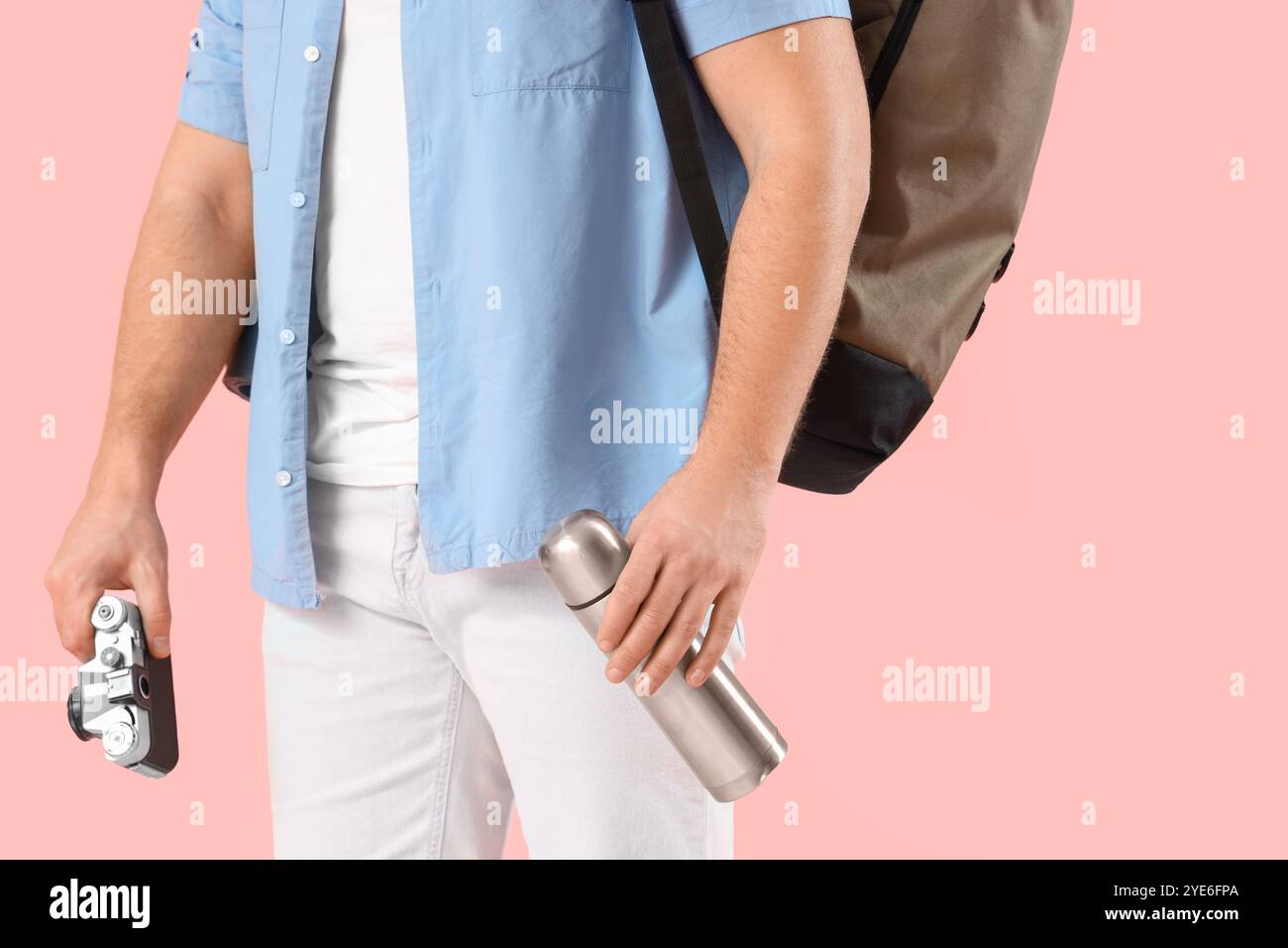 Turista maschile con zaino, thermos e fotocamera su sfondo rosa Foto Stock