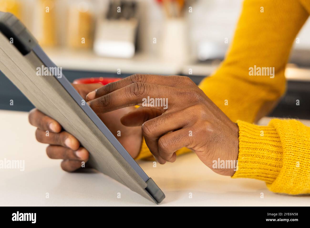 Uomo afroamericano in maglione giallo che usa il tablet a casa, concentrandosi sullo schermo Foto Stock