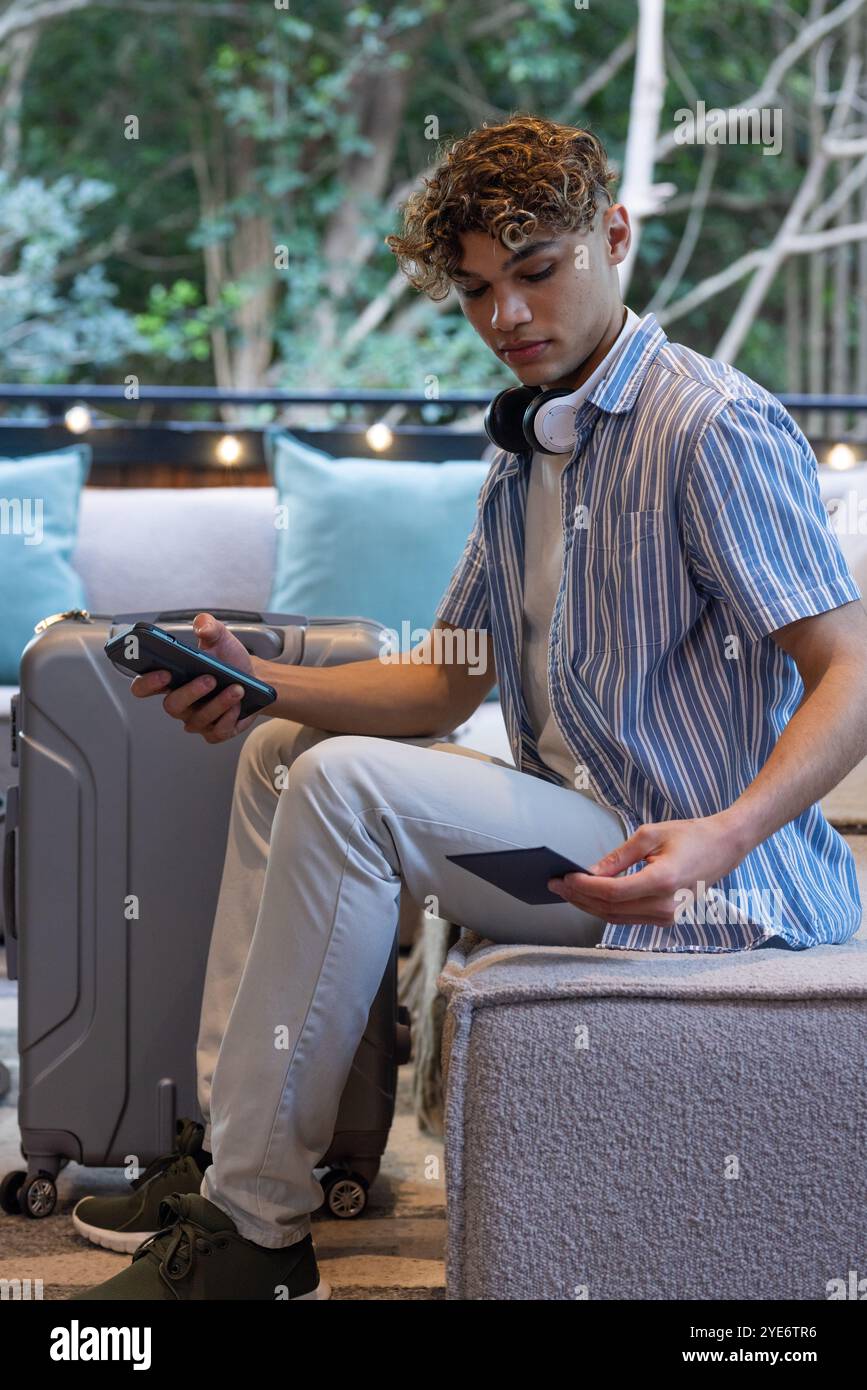 Natale, giovane con cuffie che controllano il telefono e il biglietto nella sala all'aperto, a casa Foto Stock