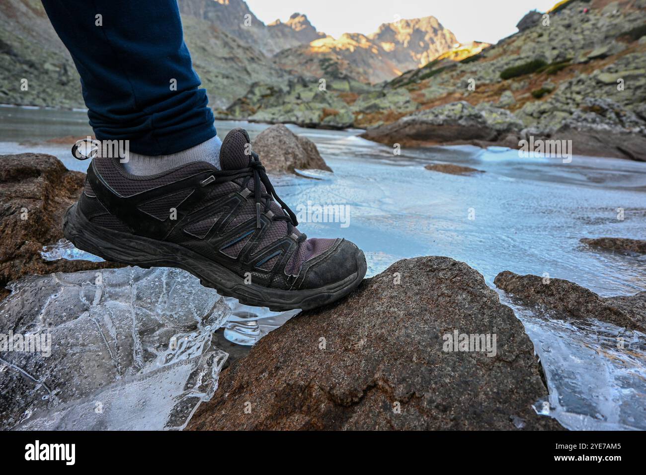 Camminate con cura mettendo i piedi su un sottile ghiaccio che copre il lago di montagna nella valle panoramica. Foto Stock