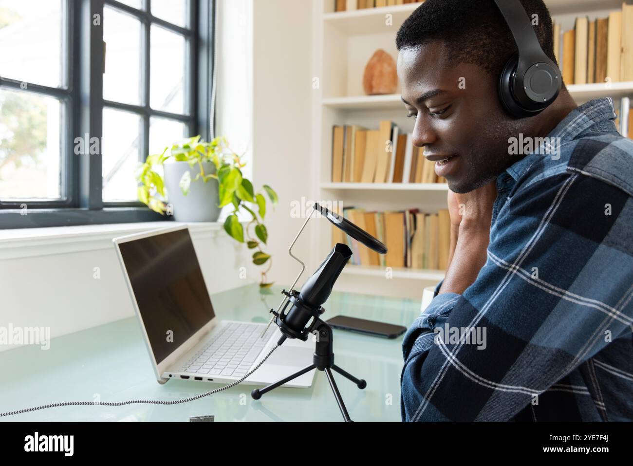 Podcasting a casa, giovane afroamericano che usa il microfono e il computer portatile e indossa le cuffie Foto Stock