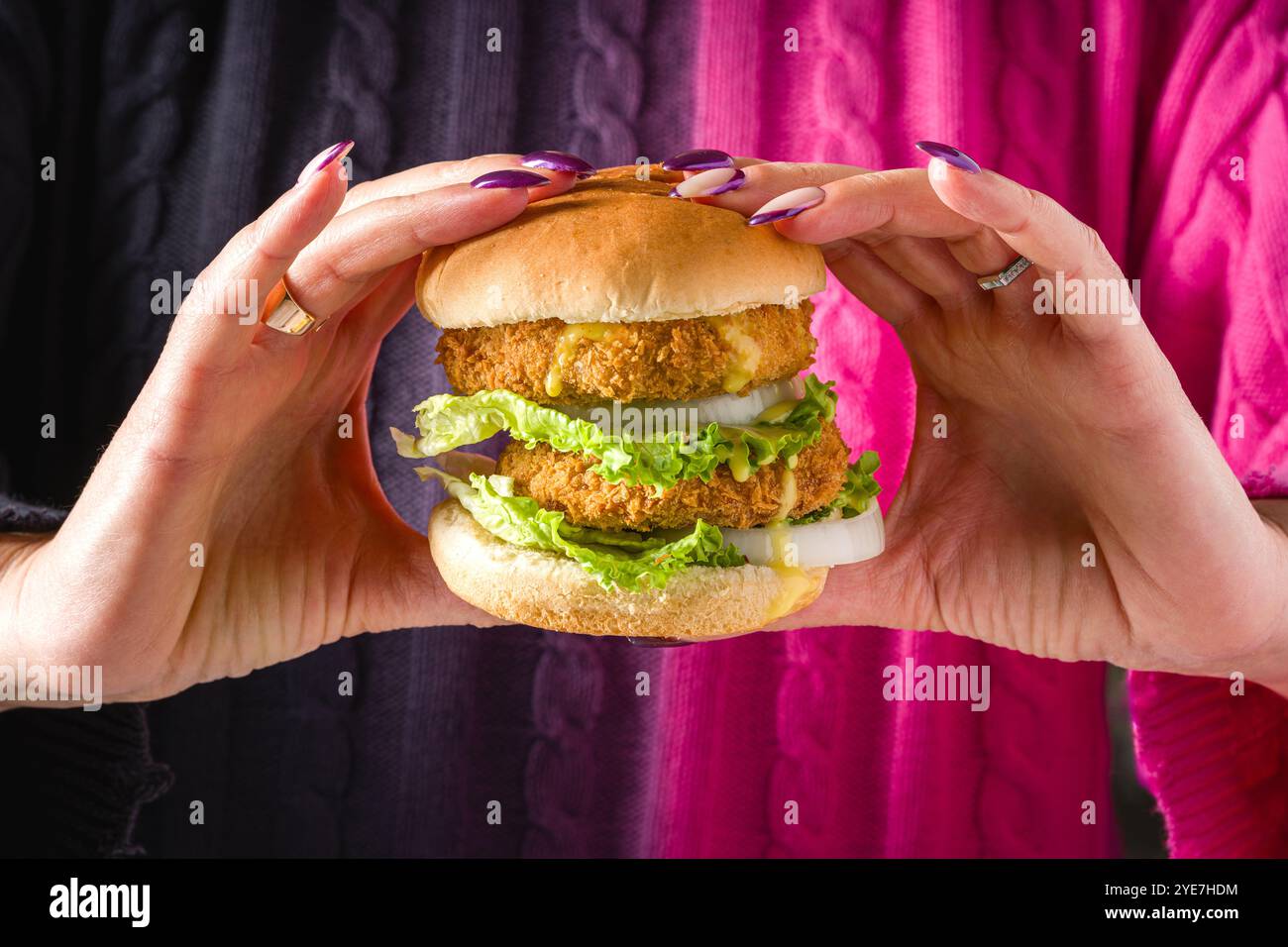 Donna che tiene con entrambe le mani un hamburger di pesce o di pollo Foto Stock