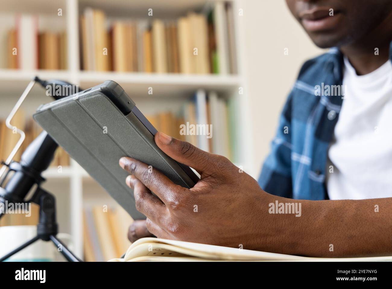 Uomo afroamericano che usa tablet e microfono a casa, concentrandosi sul lavoro Foto Stock