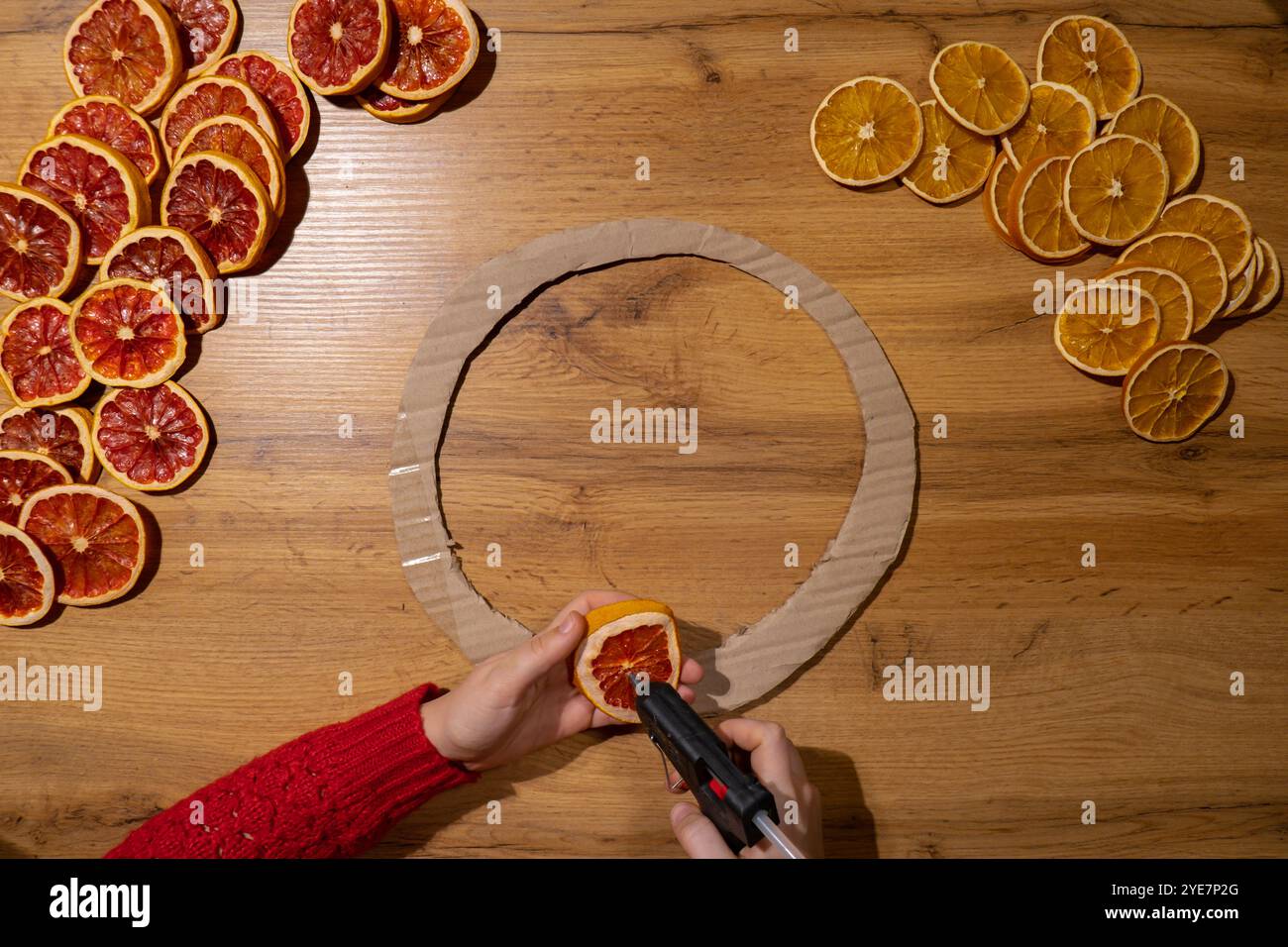 Fase 1 Corona di Natale fatta a mano da fette di pompelmo d'arancia secca. Donna che usa colla calda per preparare le feste, crea un'arte di creare decorazioni creative. Attività pratiche creazione di un workshop di regali per le festività sostenibili e responsabili. Vista dall'alto, disposizione piatta Foto Stock