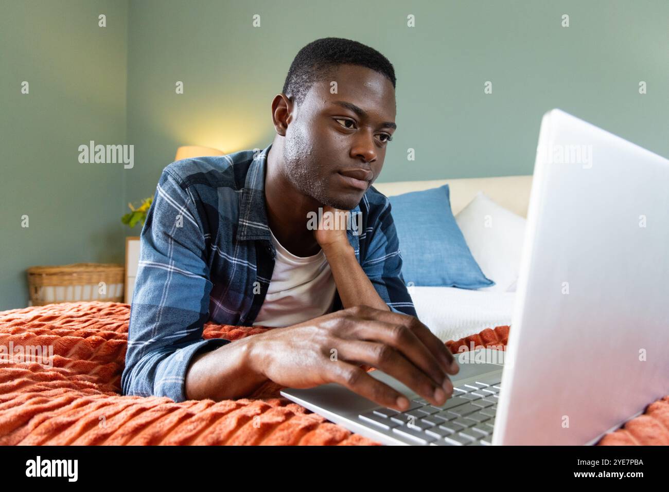Uomo afro-americano che usa un computer portatile sul letto, concentrandosi sul lavoro a casa Foto Stock