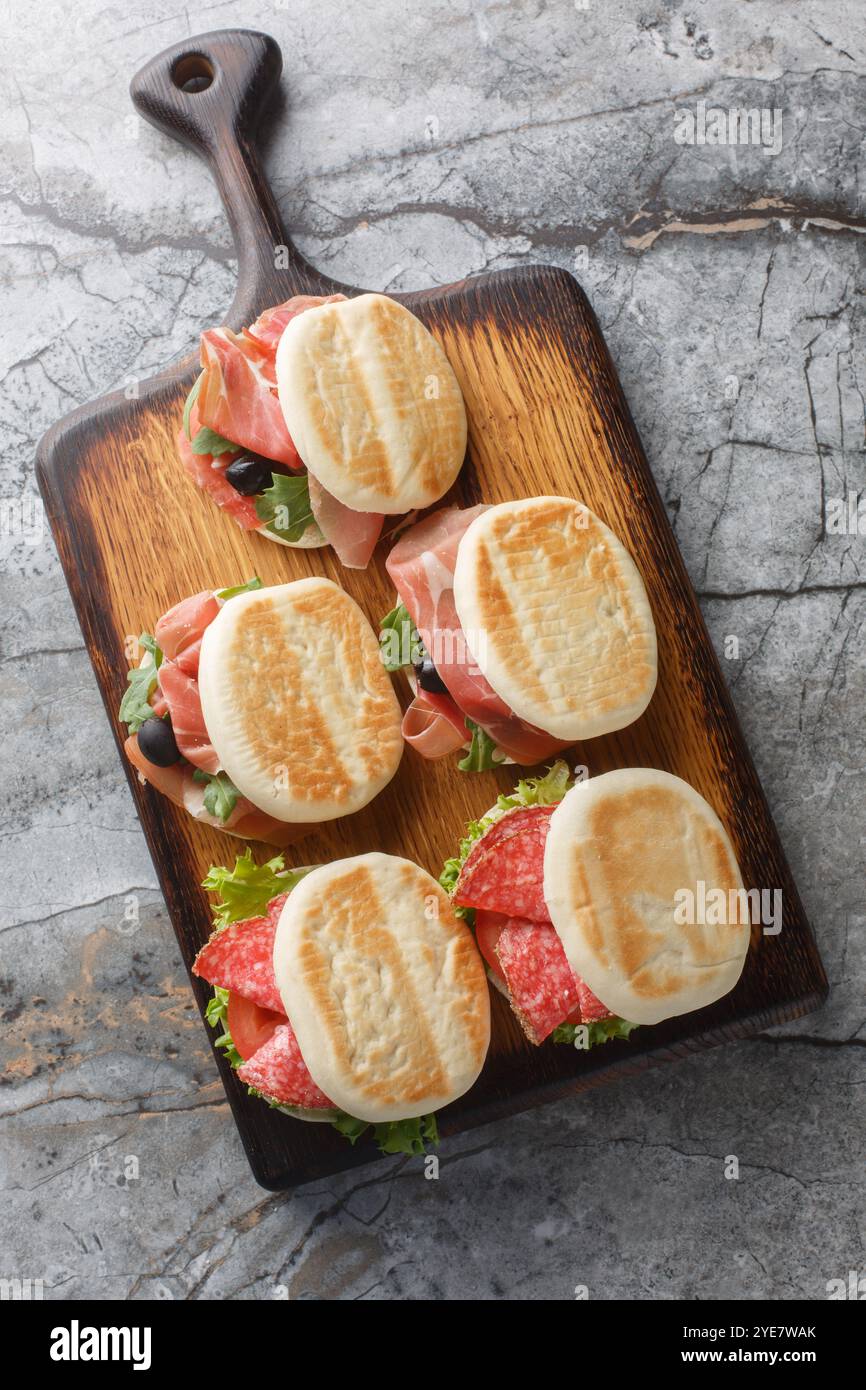 Tigelle un tipo di pane da ripieno di salame, prosciutto, olive, pomodoro, lattuga e rucola da vicino su tavola di legno. Vista dall'alto verticale da ab Foto Stock