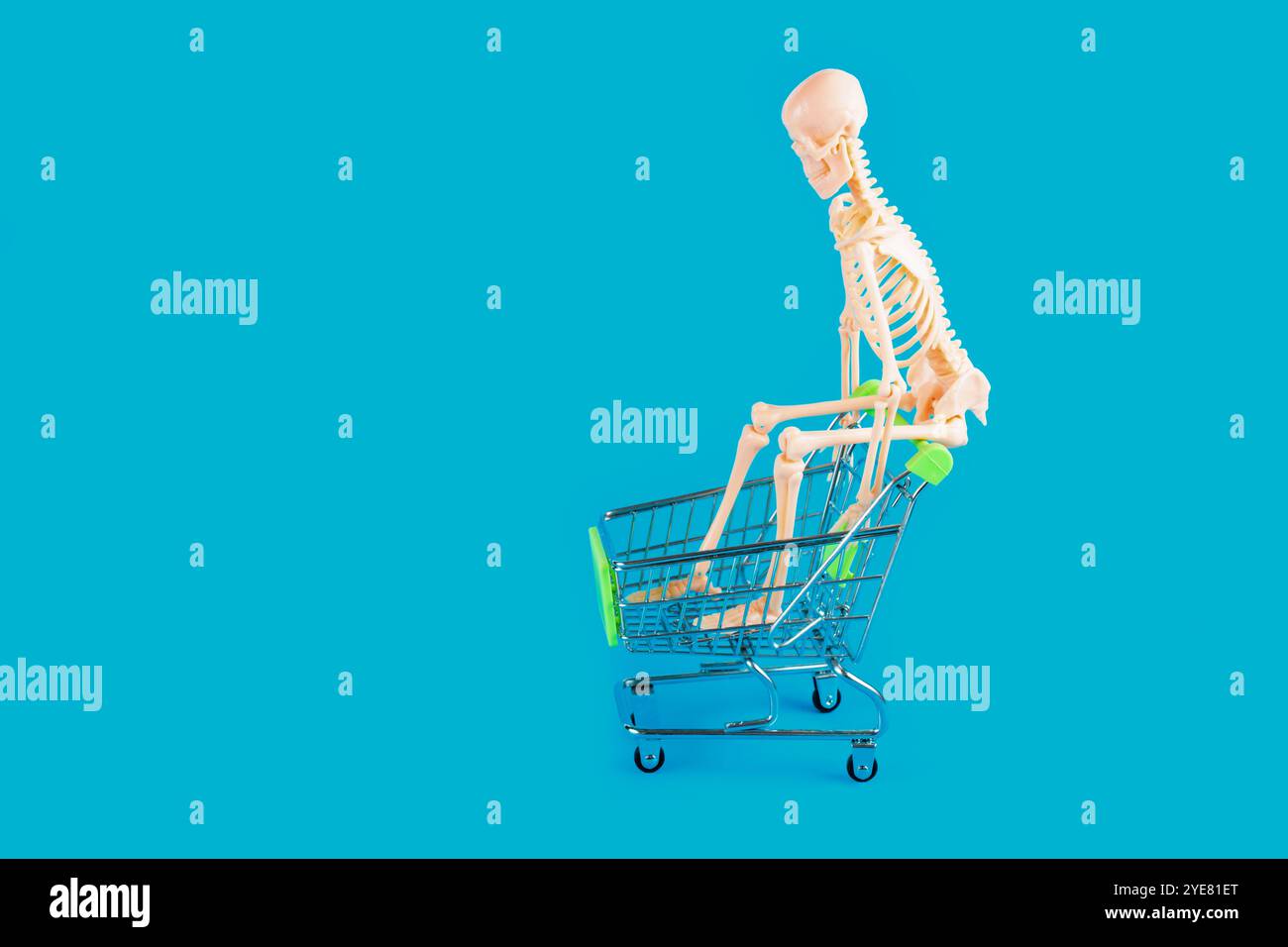 Figura scheletrica seduta all'interno di un carrello su uno sfondo blu vibrante, che simboleggia il divertimento e la creatività nello shopping. Foto Stock