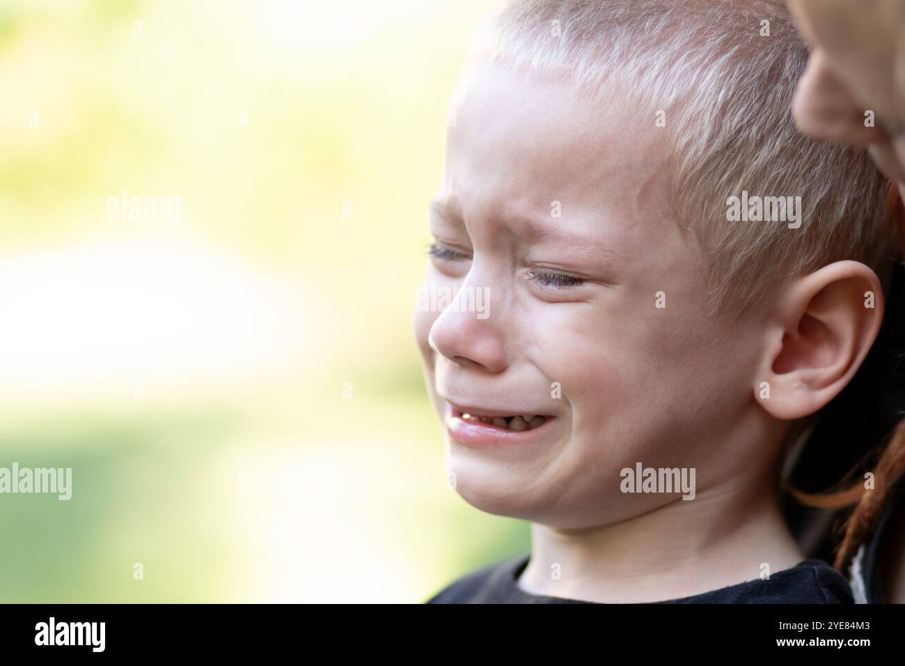 Un ritratto di un ragazzo che piange con sua madre dietro di lui Foto Stock