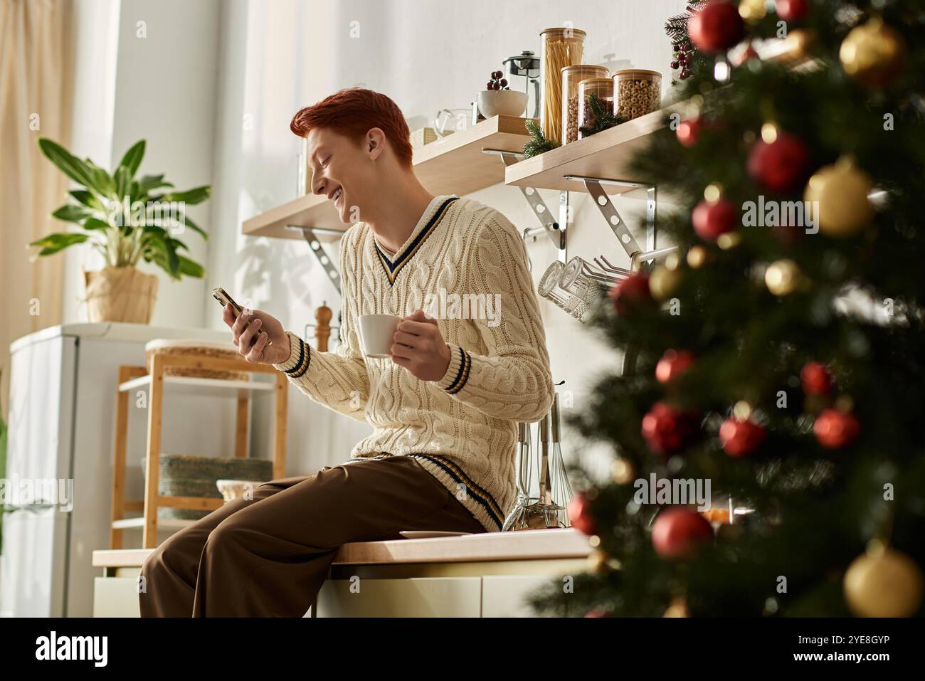 Il giovane in un comodo maglione si rilassa con una bevanda calda, celebrando la stagione delle feste. Foto Stock