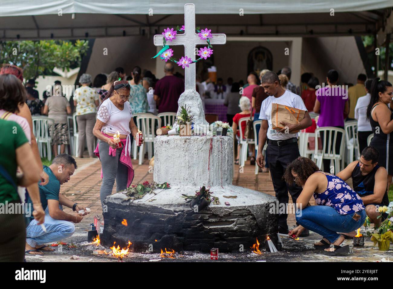 Goiania, Goias, Brasile – 2 novembre 2023: Diverse persone al cimitero recitano preghiere e accendono candele intorno a una grande croce di cemento. Foto Stock