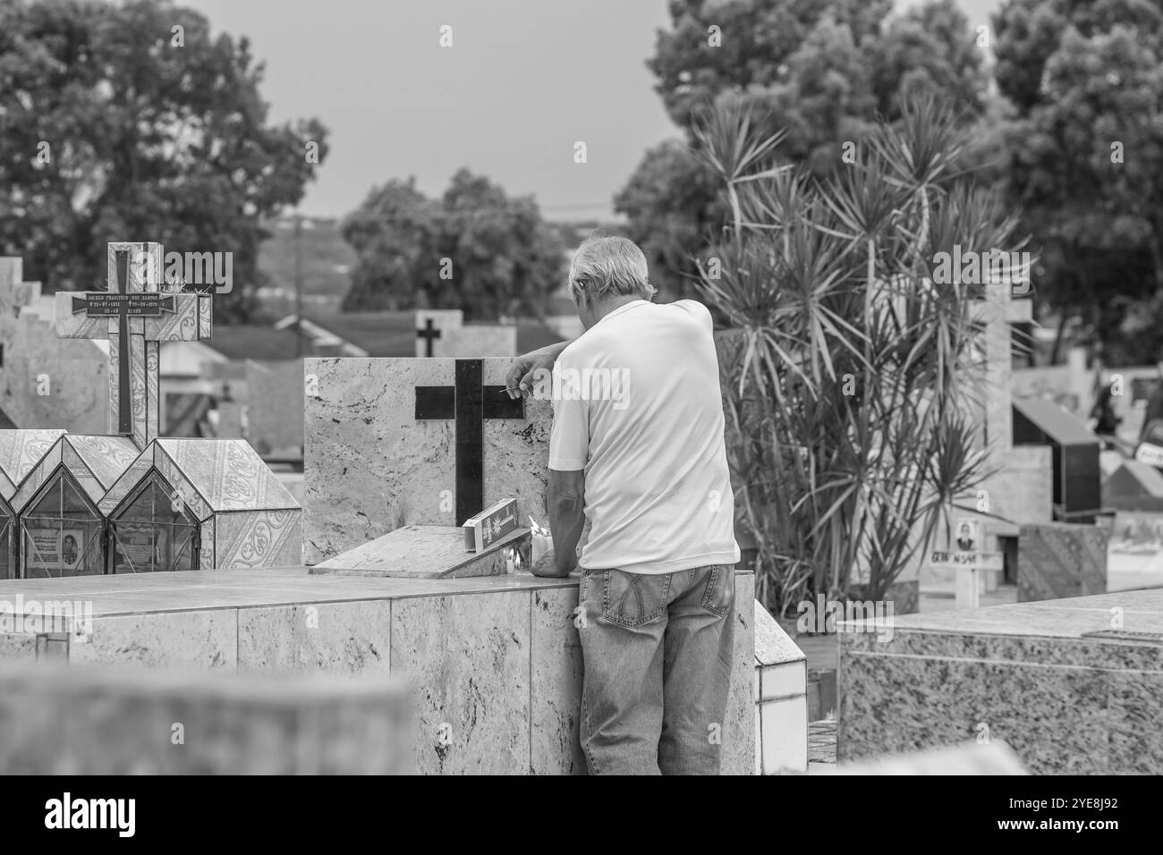 Goiania, Goias, Brasile – 2 novembre 2023: Un uomo anziano triste che accende le candele su una tomba in un cimitero. Immagine in bianco e nero. Foto Stock