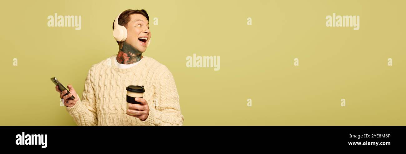 Un giovane sorride brillantemente mentre ascolta la musica, tenendo in mano un drink caldo. Foto Stock