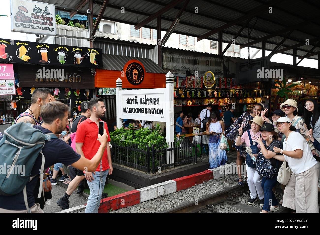 Turisti e gente del posto camminano lungo i binari ferroviari, posano e scattano foto in cellulare al mercato ferroviario, Thailandia, Mae klong Railway bangkok, Asia Foto Stock