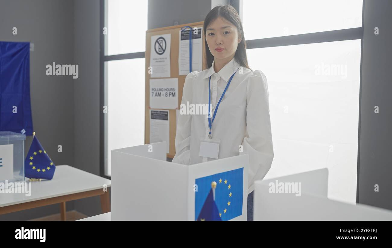 Una giovane donna asiatica segue un processo elettorale europeo in un ambiente chiuso, adornato da bandiere dell'unione europea. Foto Stock