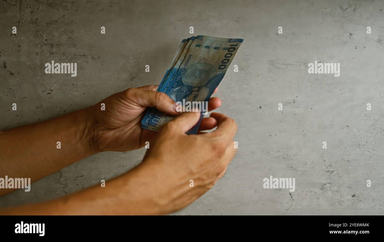 Uomo che conta pesos cileni con entrambe le mani su uno sfondo di cemento Foto Stock