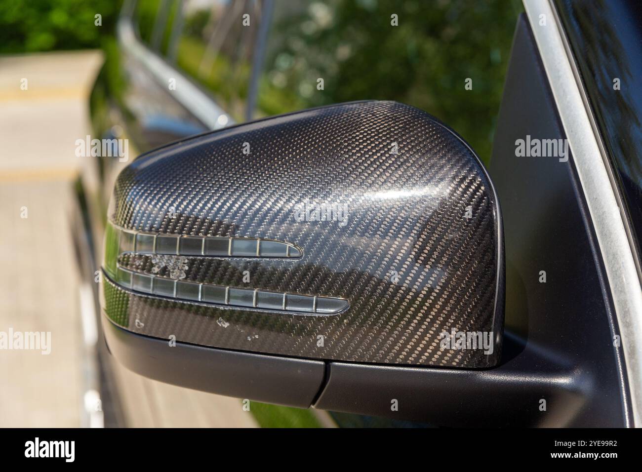 Una vista frontale dettagliata dello specchietto retrovisore nero rivestito in carbonio di un'auto, che mette in risalto il suo design elegante e i sottili rigature per un'auto autentica Foto Stock