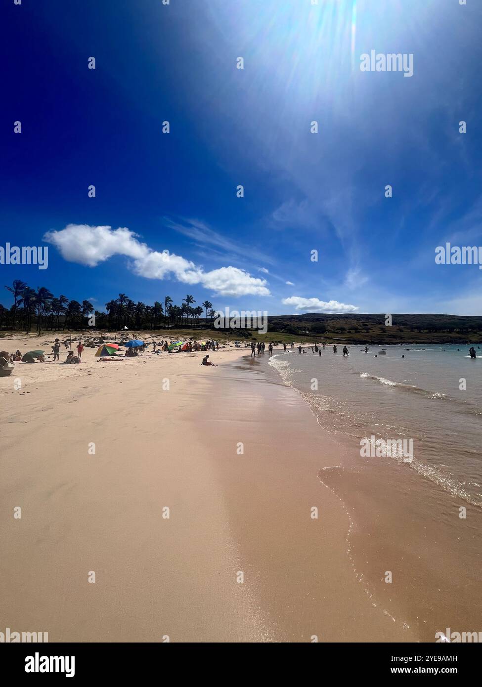 Spiaggia di Anakena sull'Isola di Pasqua, Cile, Rapa Nui, con sabbia dorata, onde calme, e tutti i visitatori si godono l'ambiente tropicale sotto un cielo blu luminoso. - Immagine stock catturata con smartphone