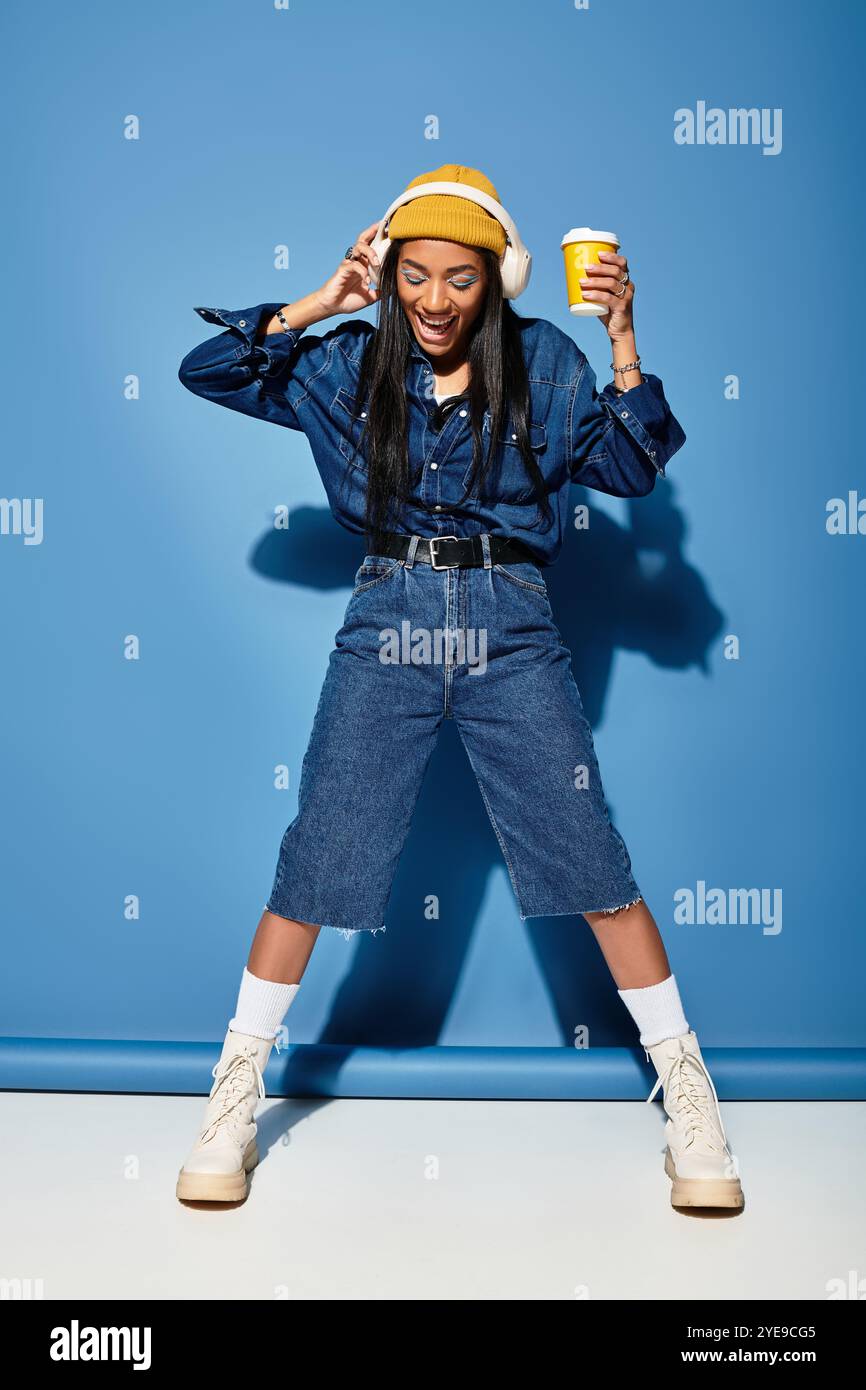 Una giovane donna sta ballando gioiosamente con un drink in mano mentre indossa abiti autunnali alla moda. Foto Stock