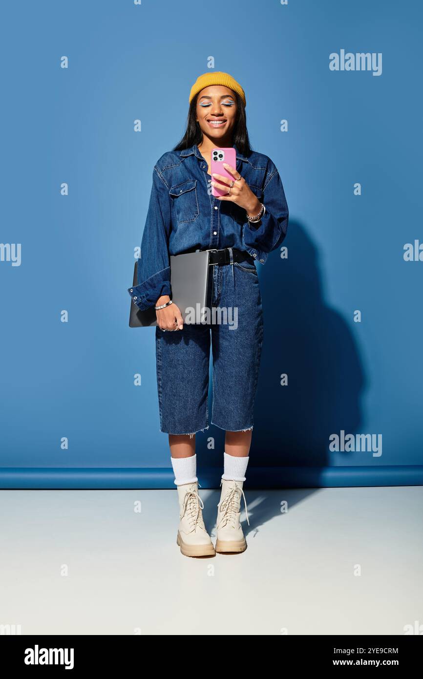 Una giovane donna con un sorriso caldo mostra il suo outfit autunnale alla moda mentre tiene in mano un telefono. Foto Stock