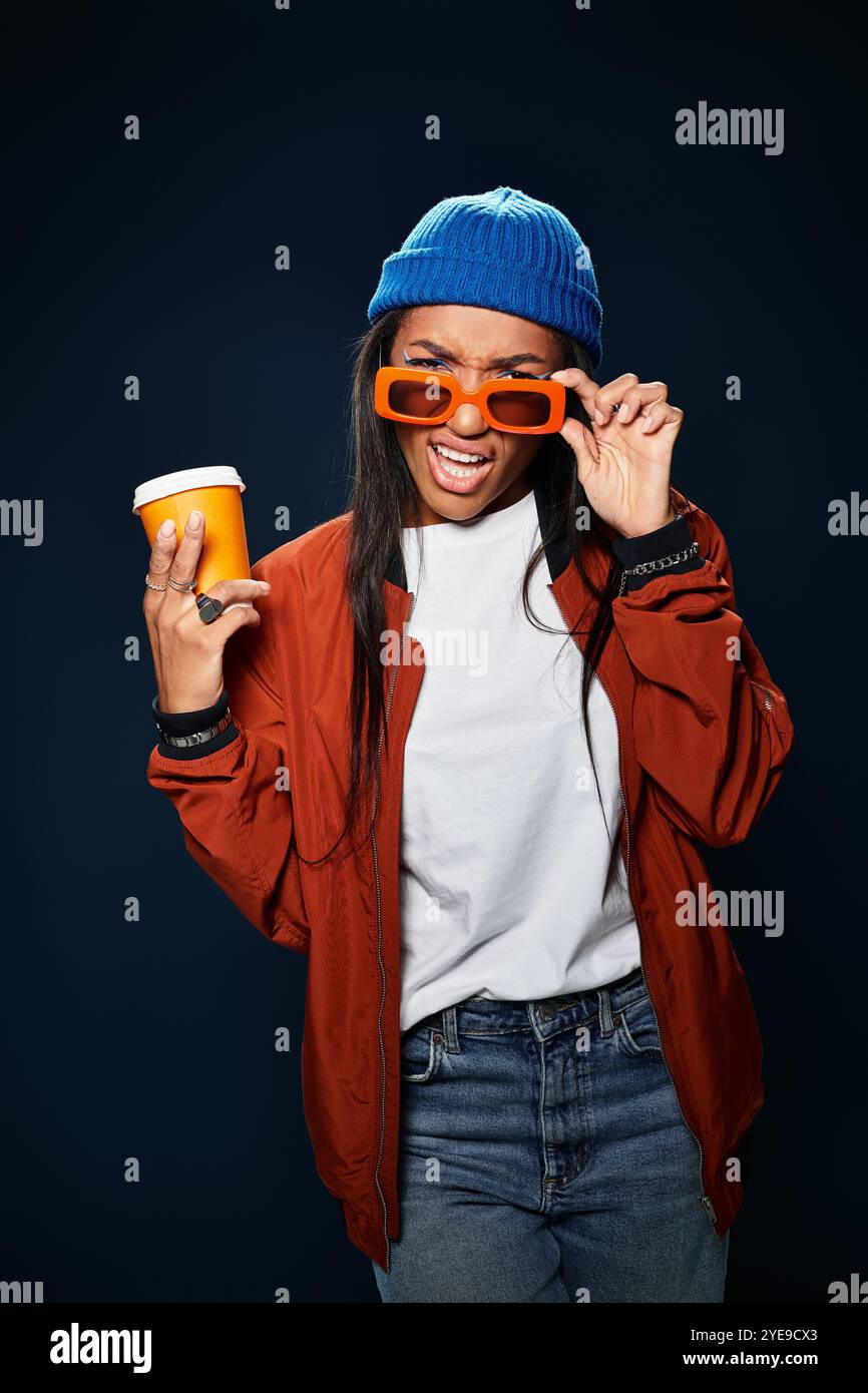 Indossando un outfit vivace, la giovane donna esprime il suo stile e il suo calore con un drink in mano. Foto Stock