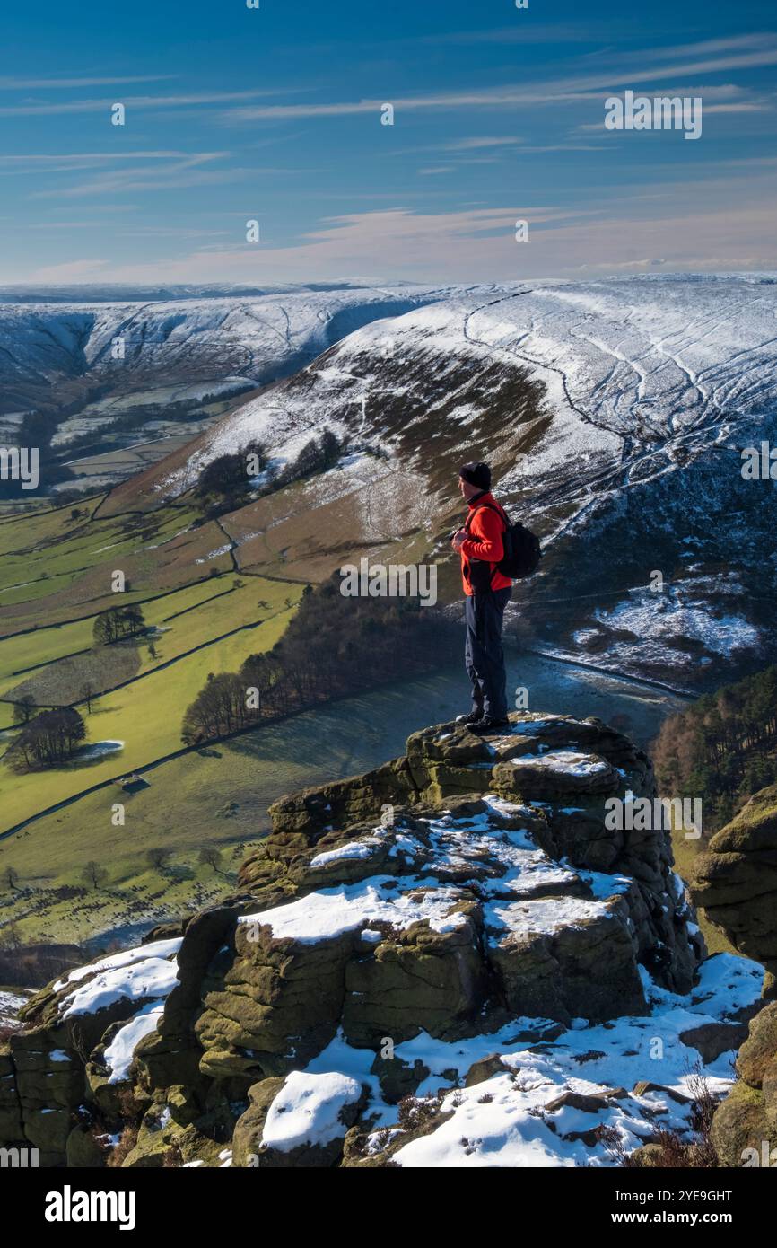 Walker si affaccia sulla Edale Valley dalla formazione rocciosa Ringing Roger in inverno, Kinder Scout, Peak District National Park, Derbyshire, Inghilterra, Regno Unito Foto Stock